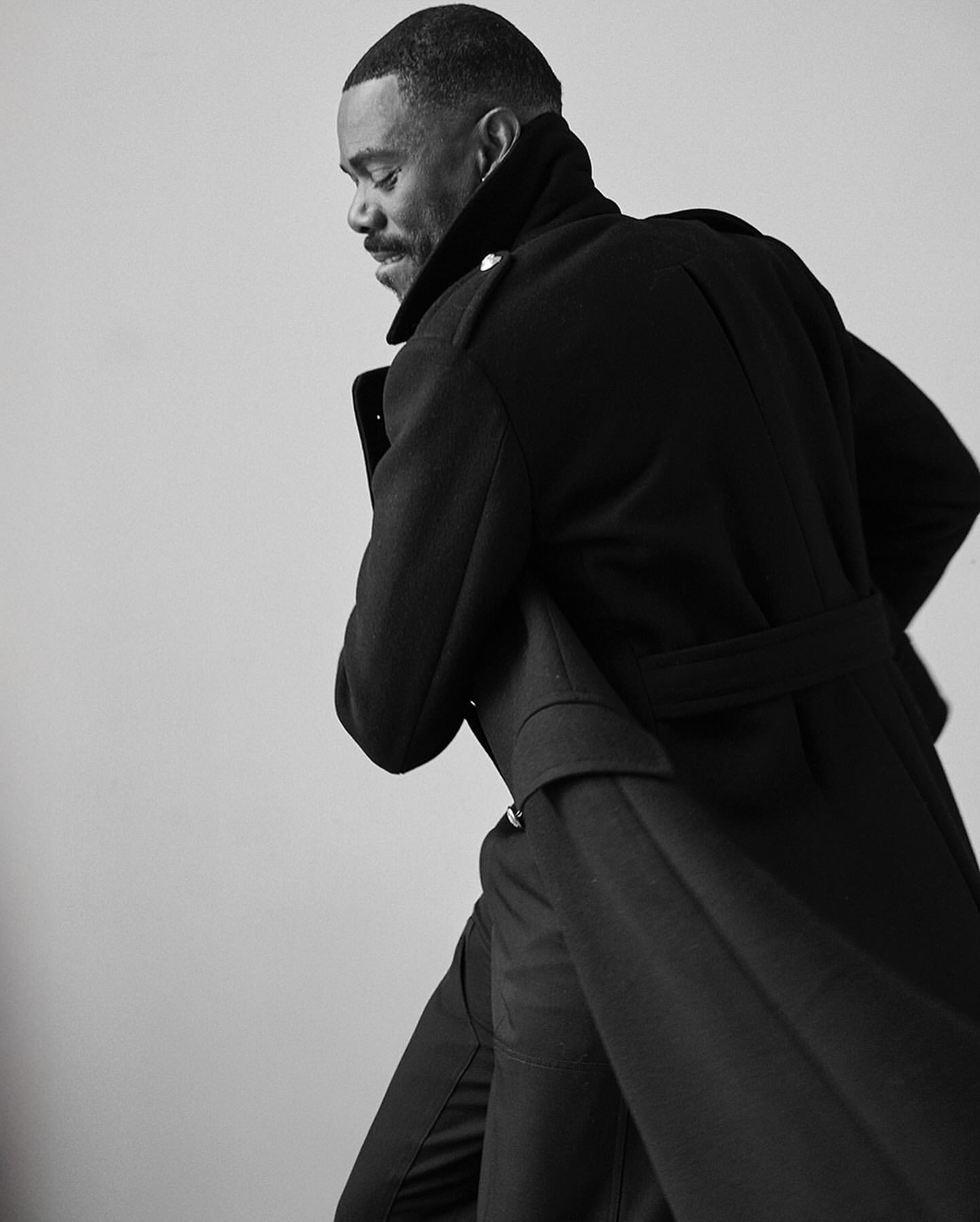 Monochrome portrait of a black man wearing a dark belted coat captured in profile by David Roemer