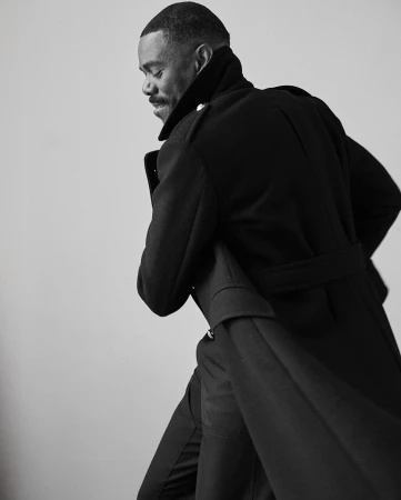Monochrome portrait of a black man wearing a dark belted coat captured in profile by David Roemer