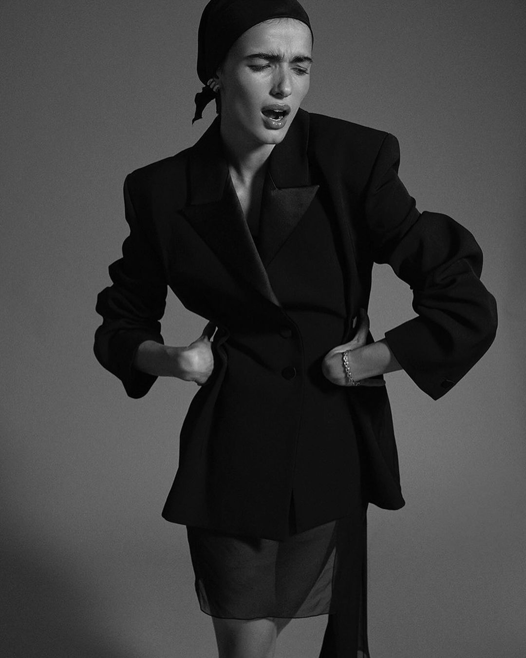 Model in a black blazer and headscarf posing against a grey studio background in Paris by David Roemer.