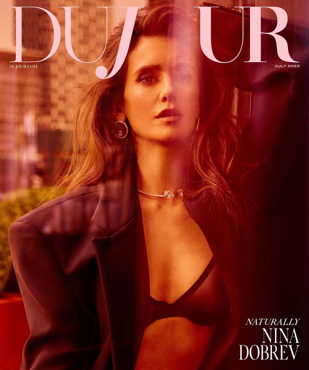 Portrait of Nina Dobrev on a magazine cover, wearing a blazer and necklace, posing with a serious expression against a blurred background.