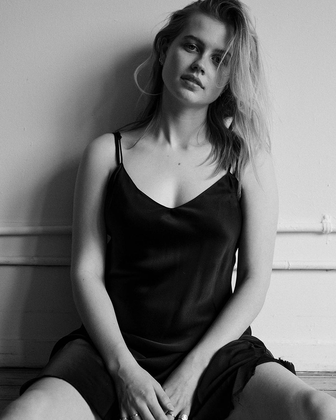 Portrait of a woman wearing a dark silk slip dress sitting against an interior wall with molding lines, photographed by David Roemer.