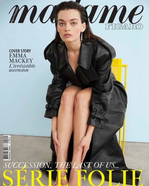 Emma Mackey poses in a black leather trench coat on a yellow chair for Madame Figaro magazine cover with a light blue background.