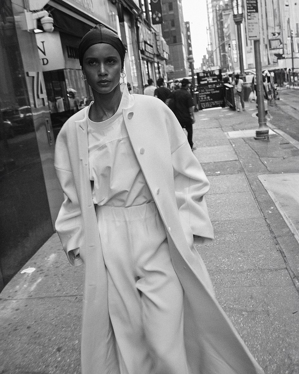 Model wearing a long coat and headscarf walking down a city street, captured in black and white by David Roemer in Paris.