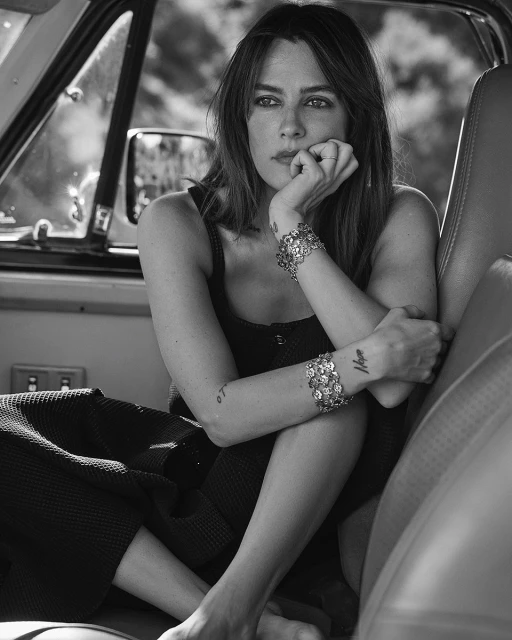 Black-and-white portrait of an adult female with bracelets sitting inside a vehicle, lit with natural light.