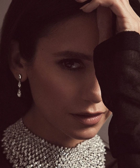 Close-up portrait of an adult woman wearing a statement diamond necklace and teardrop earrings, with soft lighting and dark background.