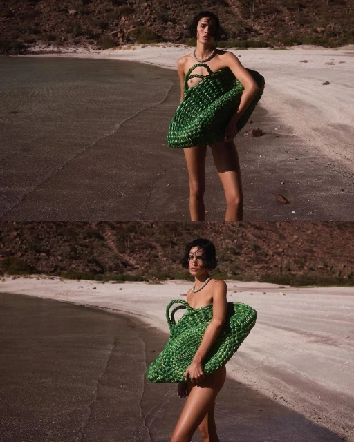 Fashion shot of a woman in swimwear on a beach holding a green woven bag. The background features an ocean and a mountain.