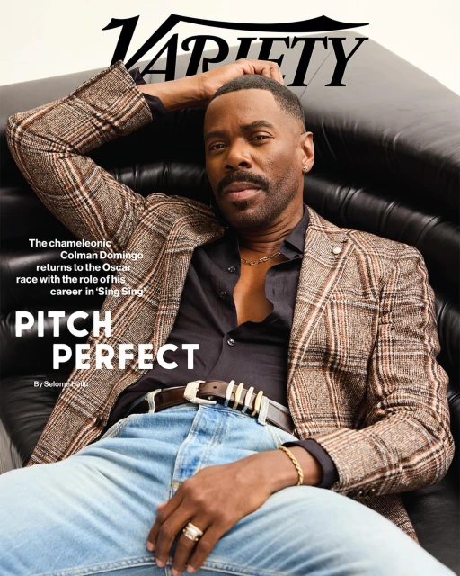 Colman Domingo poses on a black leather couch on the Variety cover, wearing a plaid blazer, jeans, and gold jewelry. 