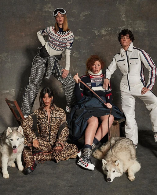 Four fashion models pose with two Husky dogs against a mottled grey backdrop, wearing patterned ski apparel by Christian Dior.