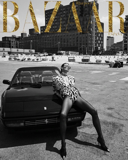 Fashion editorial with a woman in a leopard print bodysuit posing on a black Ferrari convertible in an urban setting with buildings.