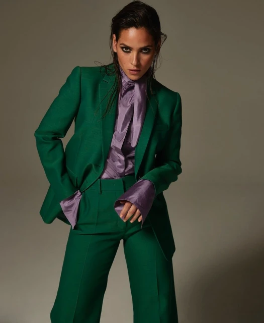 Brunette woman in a green suit and lavender silk blouse poses against a grey backdrop in a fashion forward studio portrait.