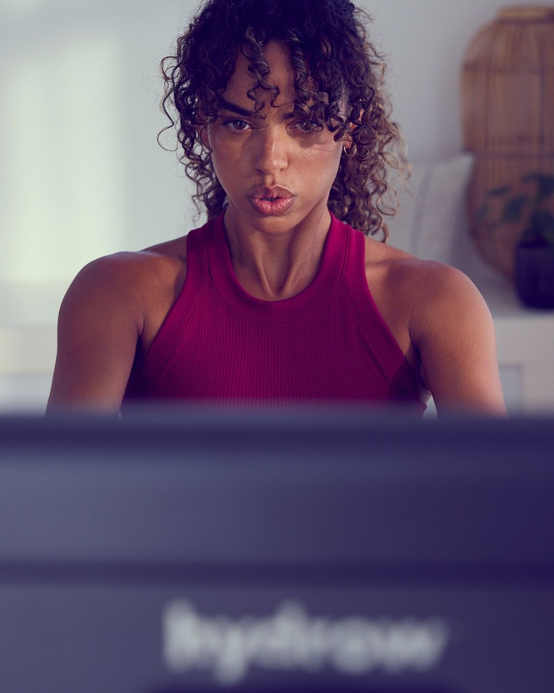 Focused woman in burgundy workout top exercises at home on indoor training equipment in a fitness and wellness context.