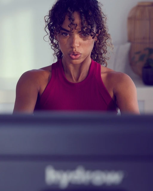 Focused woman in burgundy workout top exercises at home on indoor training equipment in a fitness and wellness context.