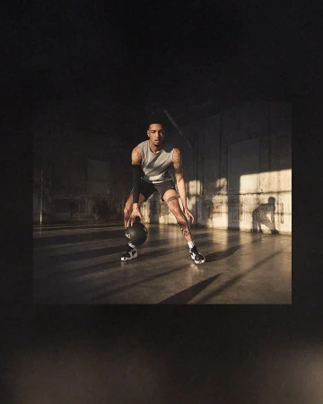 A male athlete in sportswear dribbles a basketball on a polished court, with a concentrated expression and natural light illuminating the scene.