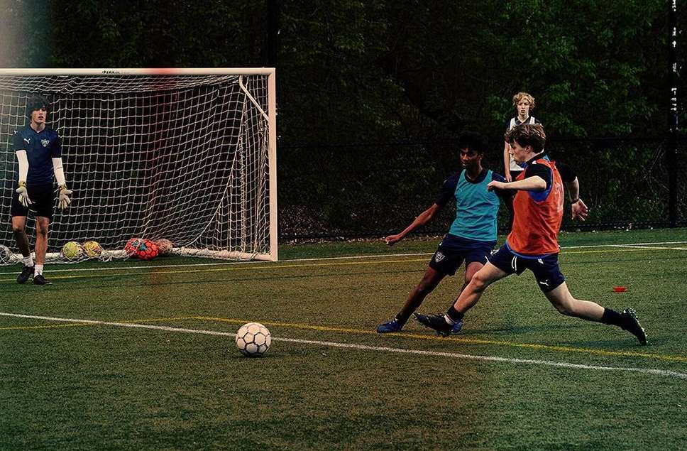 Youth soccer game on a green field featuring young players in action, a soccer ball in play, and a goal with netting.