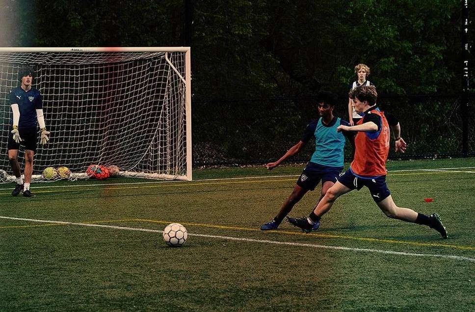 Youth soccer game on a green field featuring young players in action, a soccer ball in play, and a goal with netting.