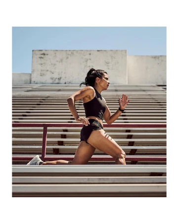Athletic woman runs on outdoor stadium steps in sports bra and shorts, viewed from a low angle on a sunny day.