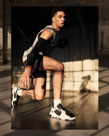 Male athlete in sportswear crouches while holding a basketball in a gritty indoor environment with strong directional lighting.