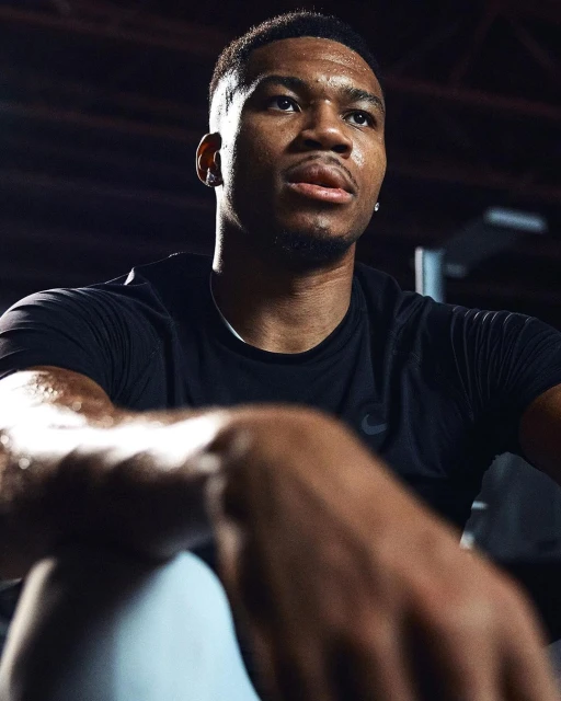 Close-up studio shot of a sweaty adult male athlete in black activewear looking up; portrait orientation, dark background.