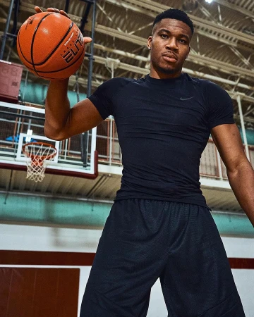 Adult male basketball player holding an orange basketball in an indoor court with a hoop and backboard.