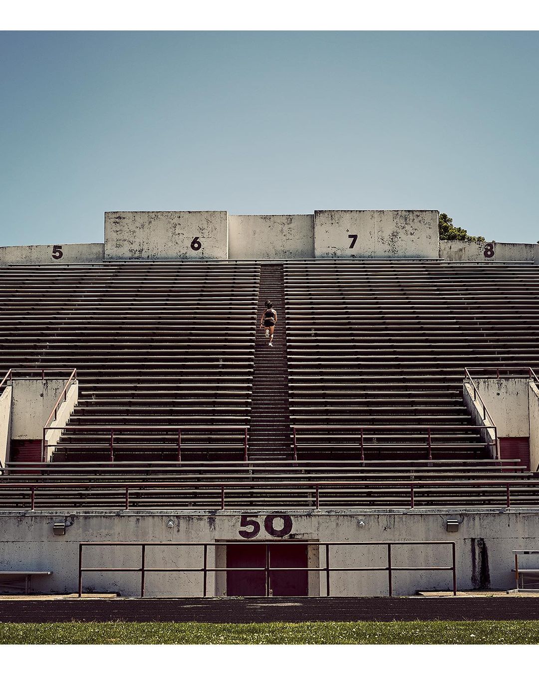 Person climbs the concrete steps of a stadium bleacher section beneath a clear sky on a sunny day, athletic training.