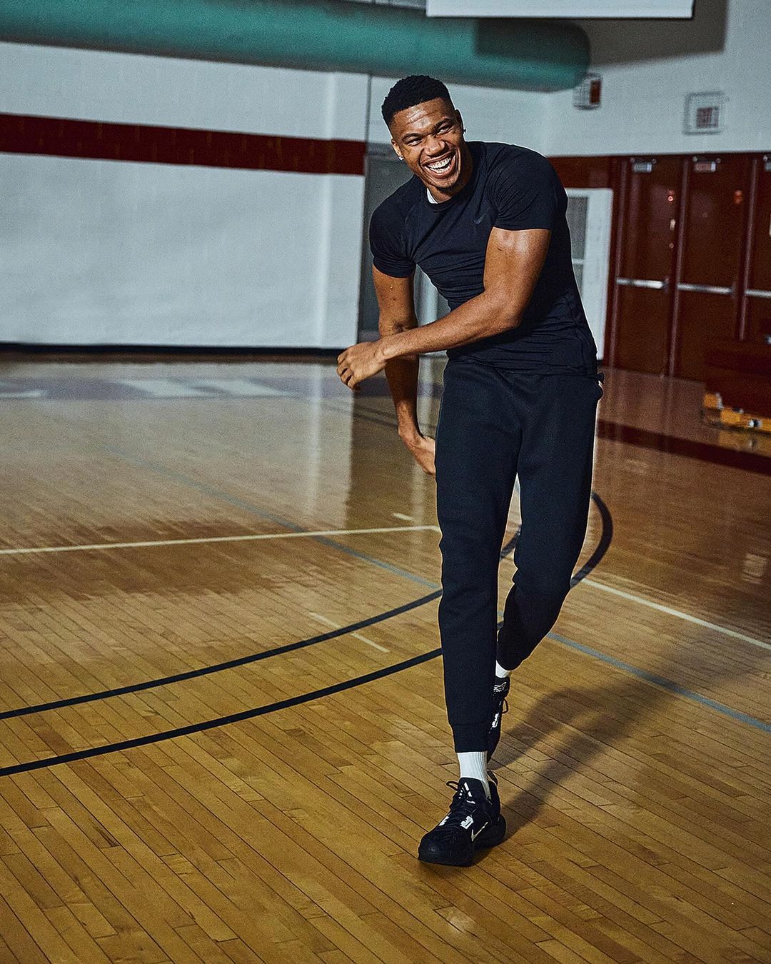Smiling adult male athlete in sports clothing and athletic shoes stands on a basketball court with wooden flooring.