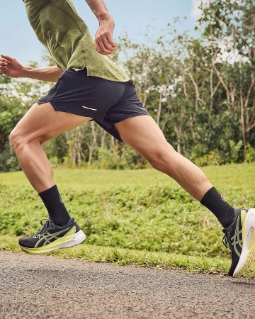 Close-up action shot of a runner wearing dark shorts, black socks, and running shoes on an outdoor path