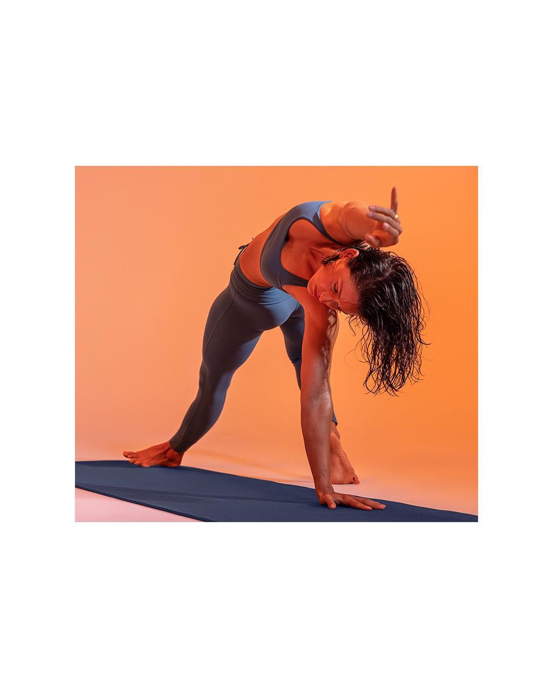 Athletic woman in blue activewear performs a yoga pose on a blue mat against an orange background, showcasing strength and flexibility.