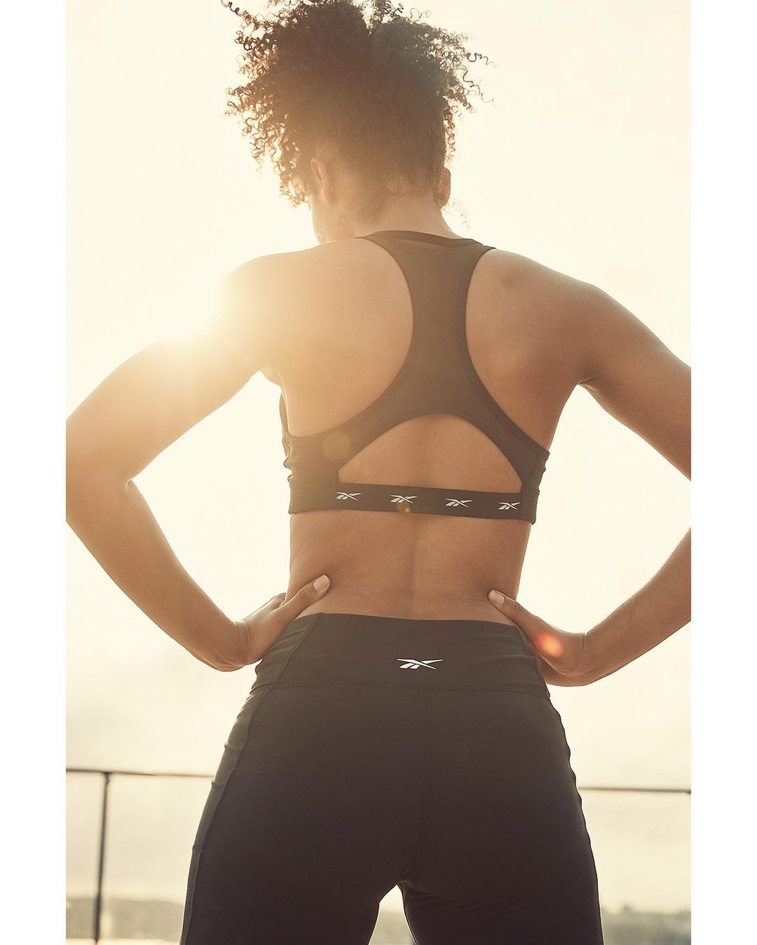Athletic woman in sports bra and leggings faces away from camera in bright sunlight. Fitness and activewear apparel for exercise.