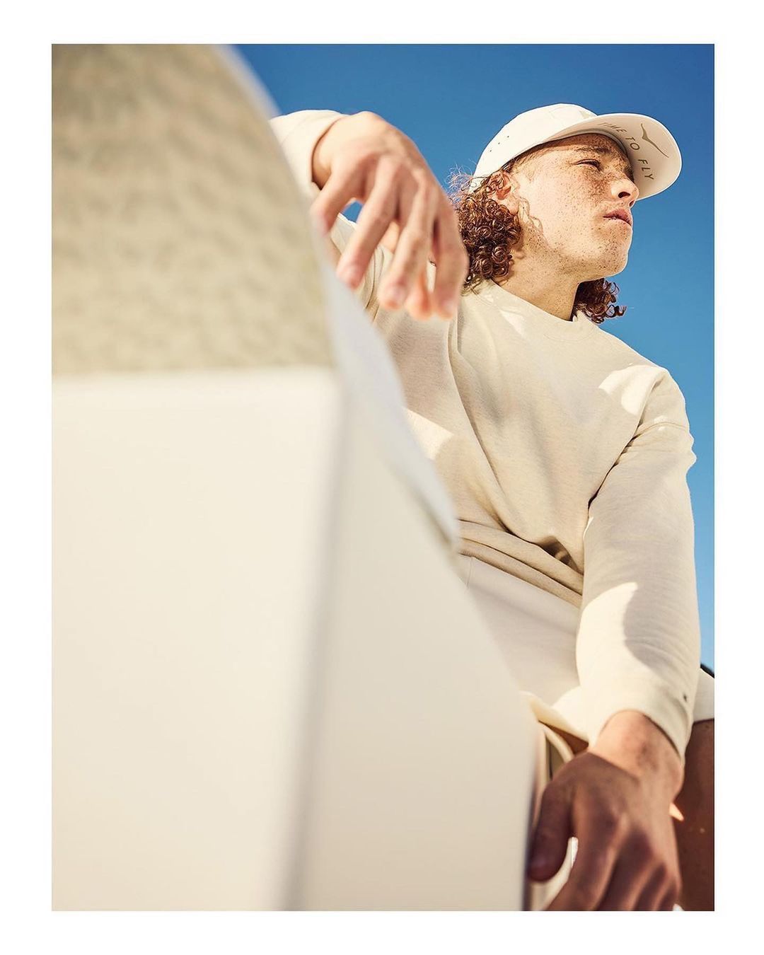 Adult man in casual clothing and hat poses outdoors against a clear blue sky, showcasing fashion and lifestyle photography with natural light.