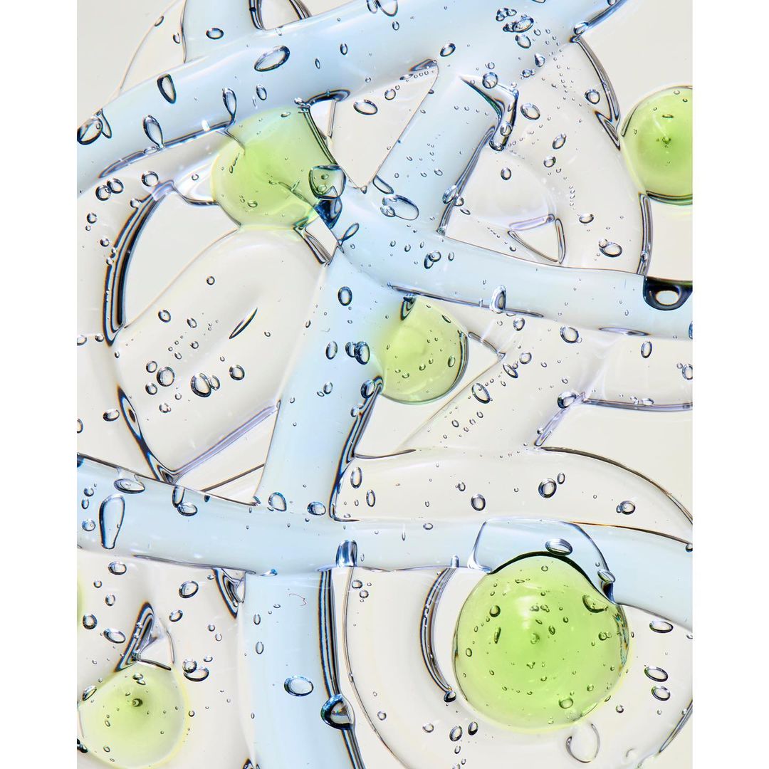 Abstract still life featuring clear and light blue gel-like tubes and spheres with water droplets against a white backdrop.