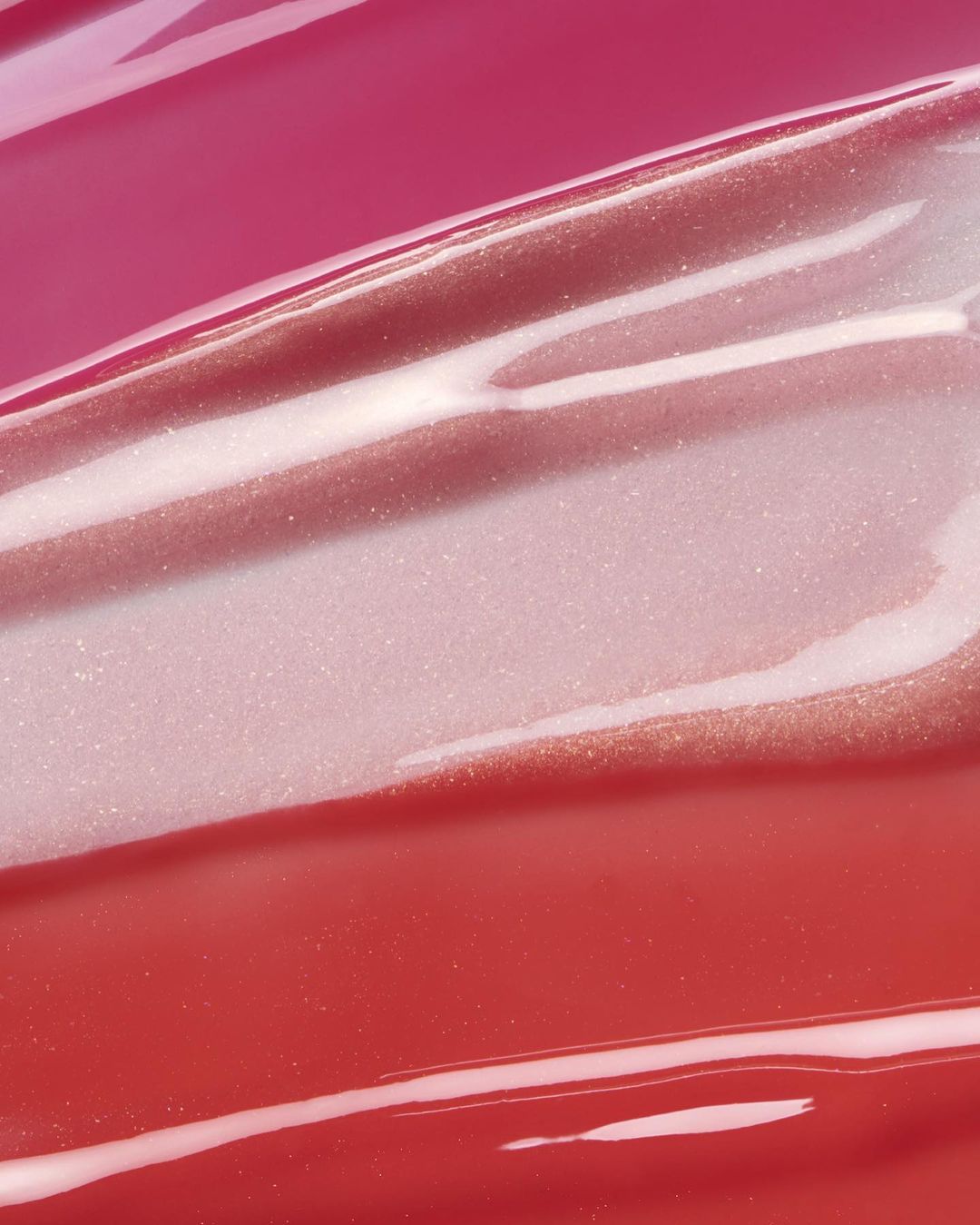 Abstract close-up of light pink, rose gold, and red glossy texture with highlights, creating a visually smooth and sparkling surface.