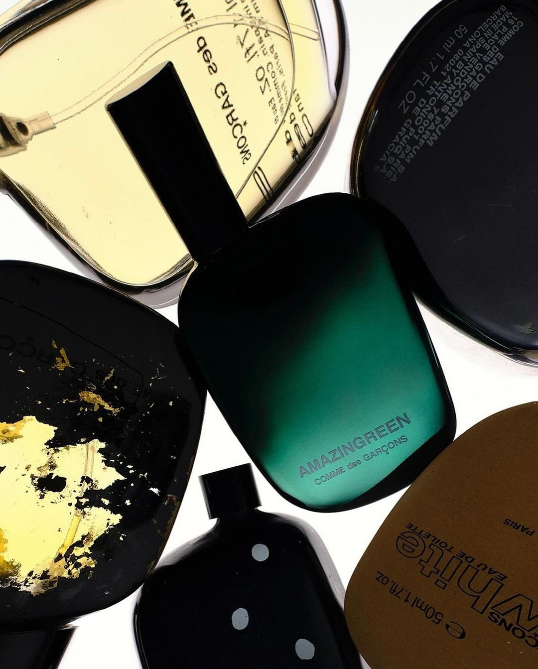Overhead shot of five perfume bottles from Comme des Garcons, showcasing various shapes, colors, and labels on a white background.