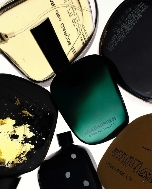 Overhead shot of five perfume bottles from Comme des Garcons, showcasing various shapes, colors, and labels on a white background.