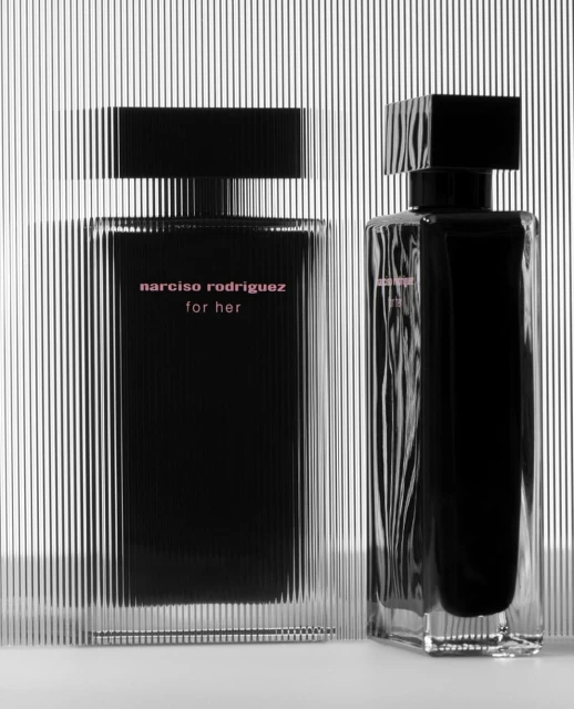 Two Narciso Rodriguez perfume bottles stand against a striped background, featuring a black and clear design with pink lettering.