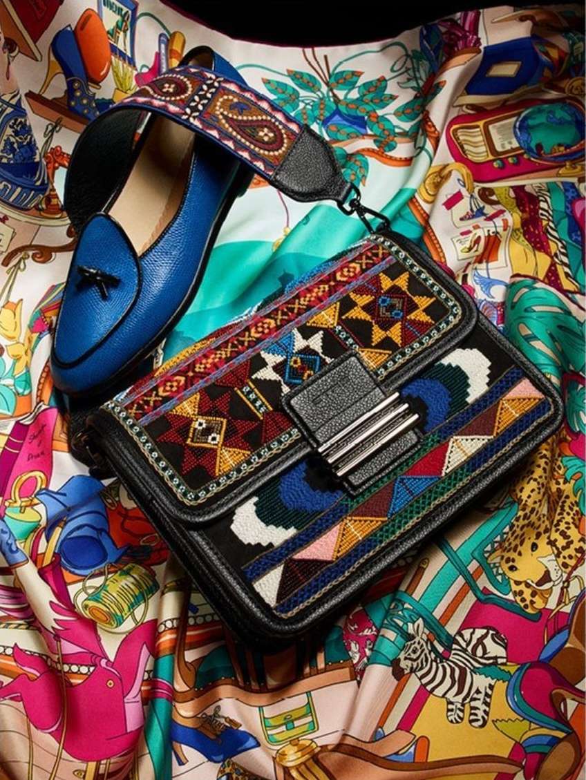 Flat lay of a blue loafer, an embroidered crossbody bag, and a patterned scarf showcasing a fashion accessories arrangement.
