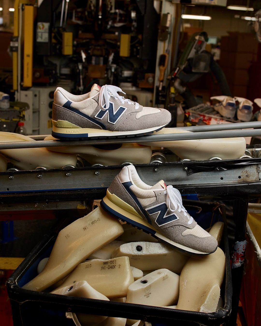 Two New Balance sneakers are displayed on a conveyor belt in a factory, emphasizing the brand's craftsmanship and manufacturing process.