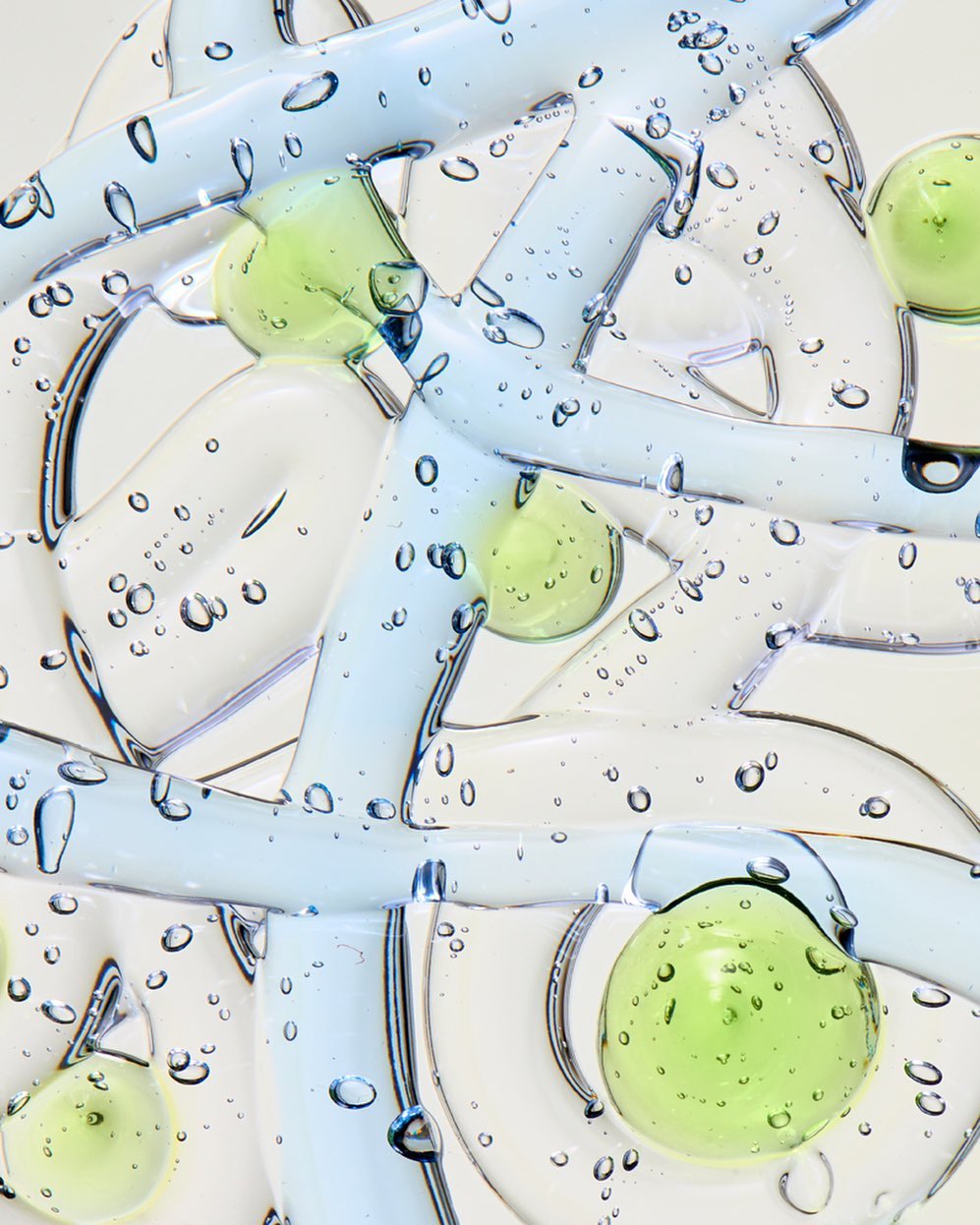 Abstract close-up of clear, blue, and green gel forms with small bubbles on a white background; beauty or healthcare product concept.
