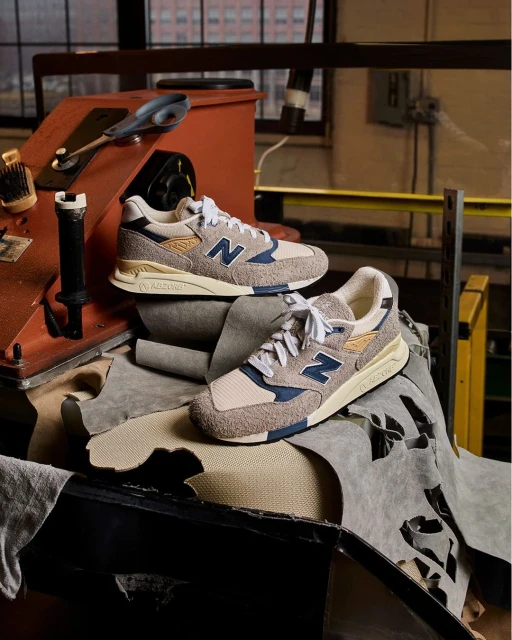 Close-up of two New Balance 998 sneakers displayed on top of leather scraps and set against a rustic industrial backdrop.