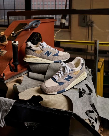 Close-up of two New Balance 998 sneakers displayed on top of leather scraps and set against a rustic industrial backdrop.