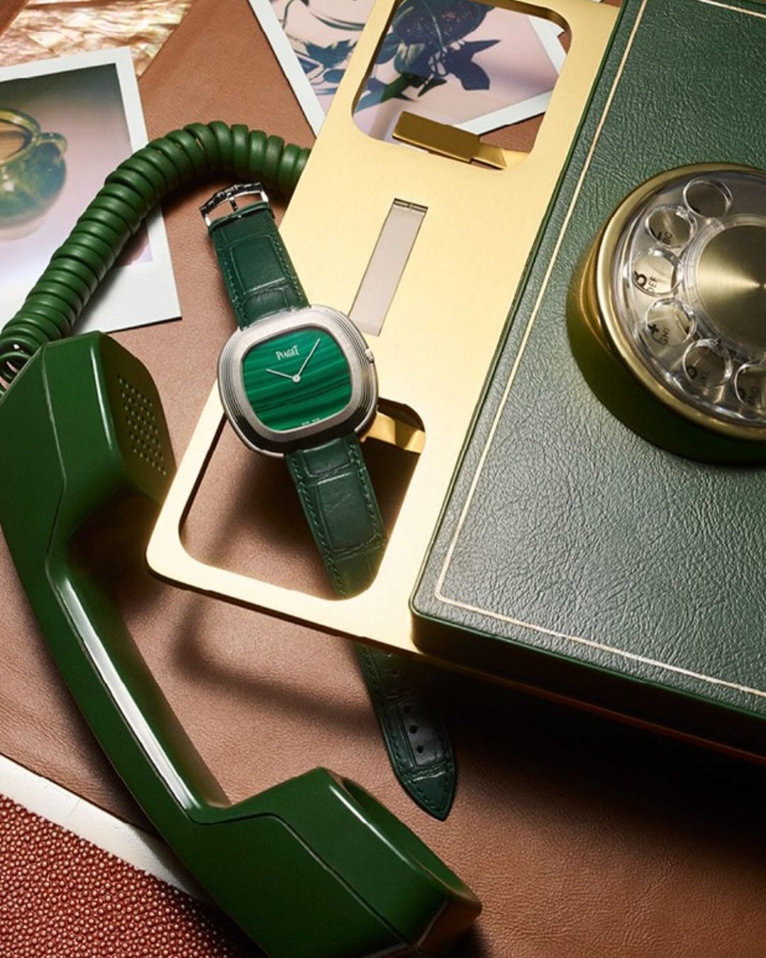 Luxury wristwatch with a malachite face and green leather strap displayed on a brown surface next to a retro green rotary telephone.