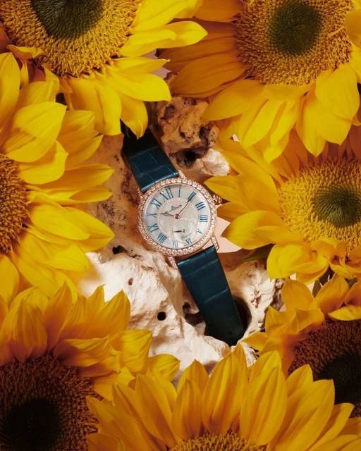 Elegant wristwatch with crystal bezel and a green leather band on cracked rock, surrounded by bright yellow sunflowers, studio setting.