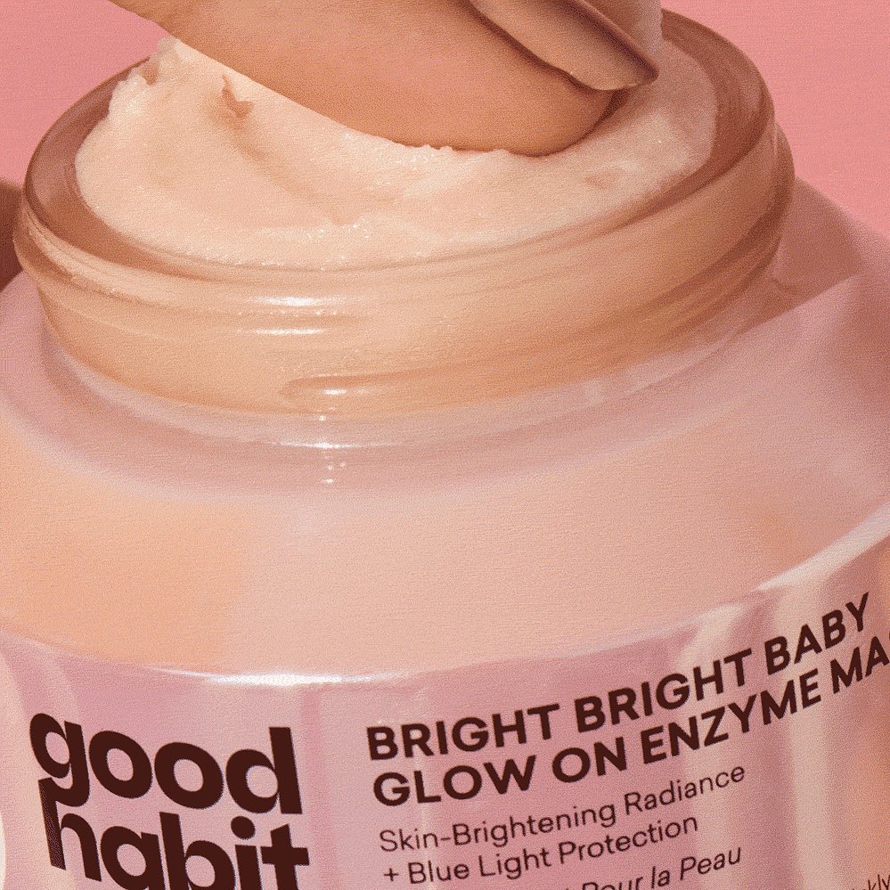 Close-up of a person's fingers scooping out light peach-colored enzyme mask from a jar of Good Habit skin-brightening radiance product.
