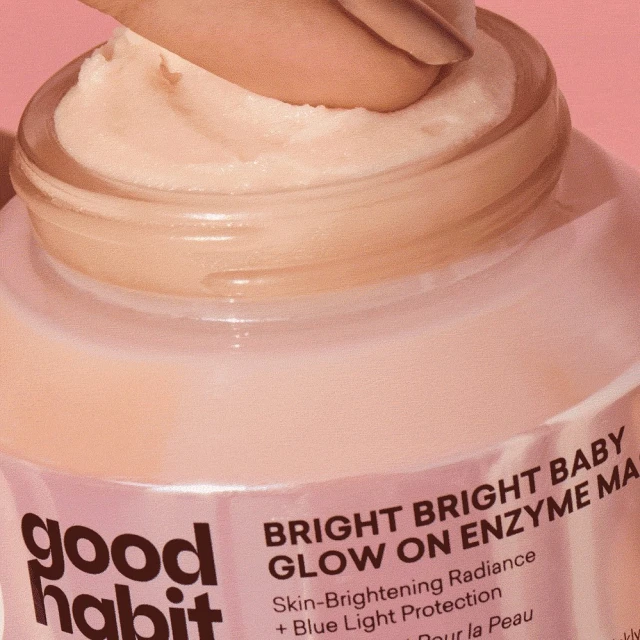 Close-up of a person's fingers scooping out light peach-colored enzyme mask from a jar of Good Habit skin-brightening radiance product.