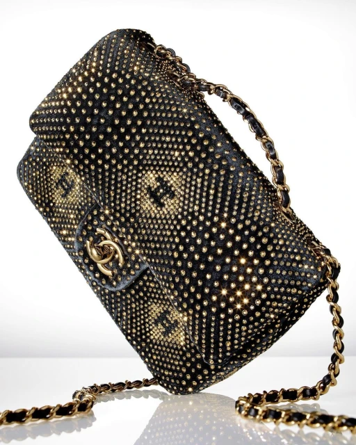 Black Chanel handbag with gold studs and chain strap on a white surface, showcasing fashion accessory with elegant design and luxury appeal.