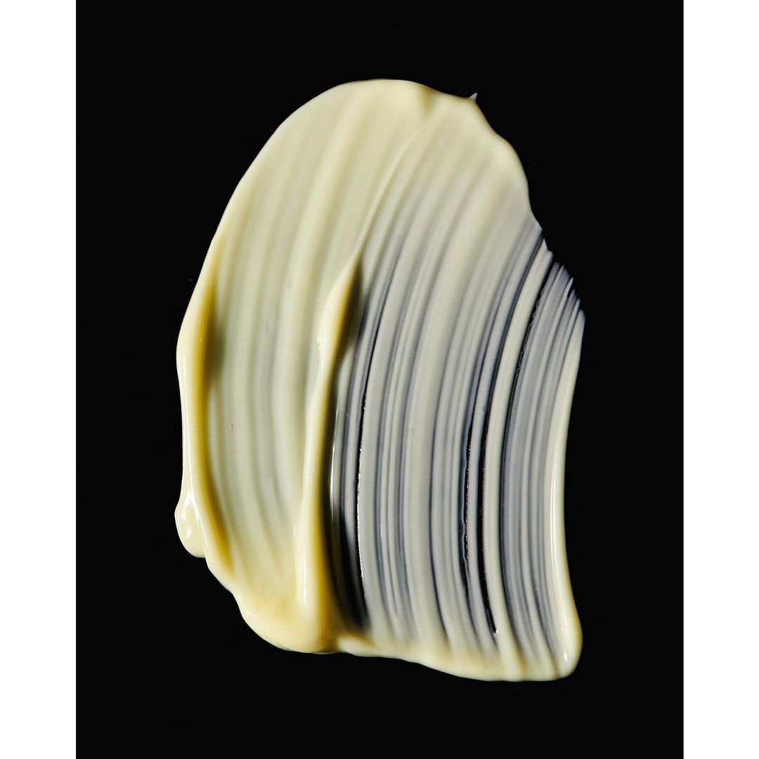 Close-up of a pale yellow cosmetic cream smear on a black background, showcasing its texture and color for beauty or skincare.