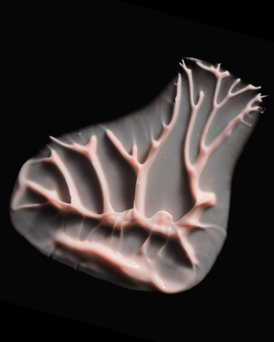 Close-up studio shot of a smear of pink cosmetic cream against a dark background, highlighting its texture and design.