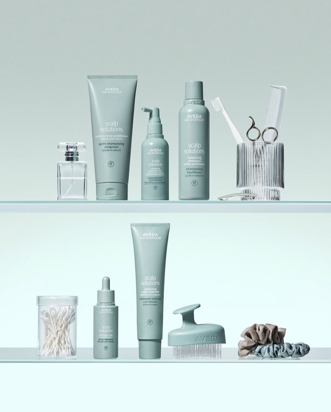 Aveda hair care products arranged on two glass shelves, featuring various scalp solution bottles, brushes, and hair accessories in a clean, minimalist setup.