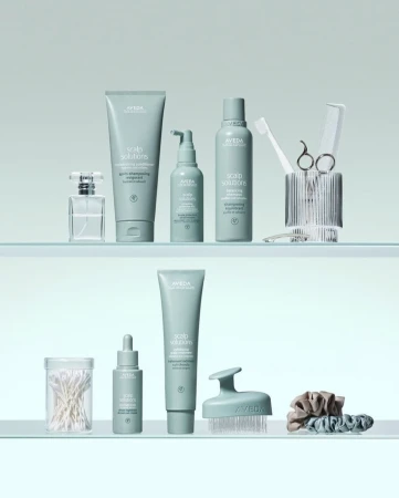 Aveda hair care products arranged on two glass shelves, featuring various scalp solution bottles, brushes, and hair accessories in a clean, minimalist setup.
