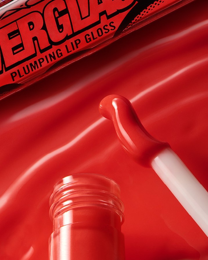 Close-up of a red lip gloss bottle with a wand applicator on a glossy red background. Beauty product advertisement for makeup.