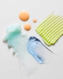 Close-up of cosmetic product swatches including blue gel, green cream, and orange drops on a white background.